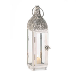 Highly polished metal highlights the intricately carved top of this stunning candle lantern. With four glass panels, a large top ring for hanging, and a fascinating door latch, this lighting accent will draw the gaze of many admirers.